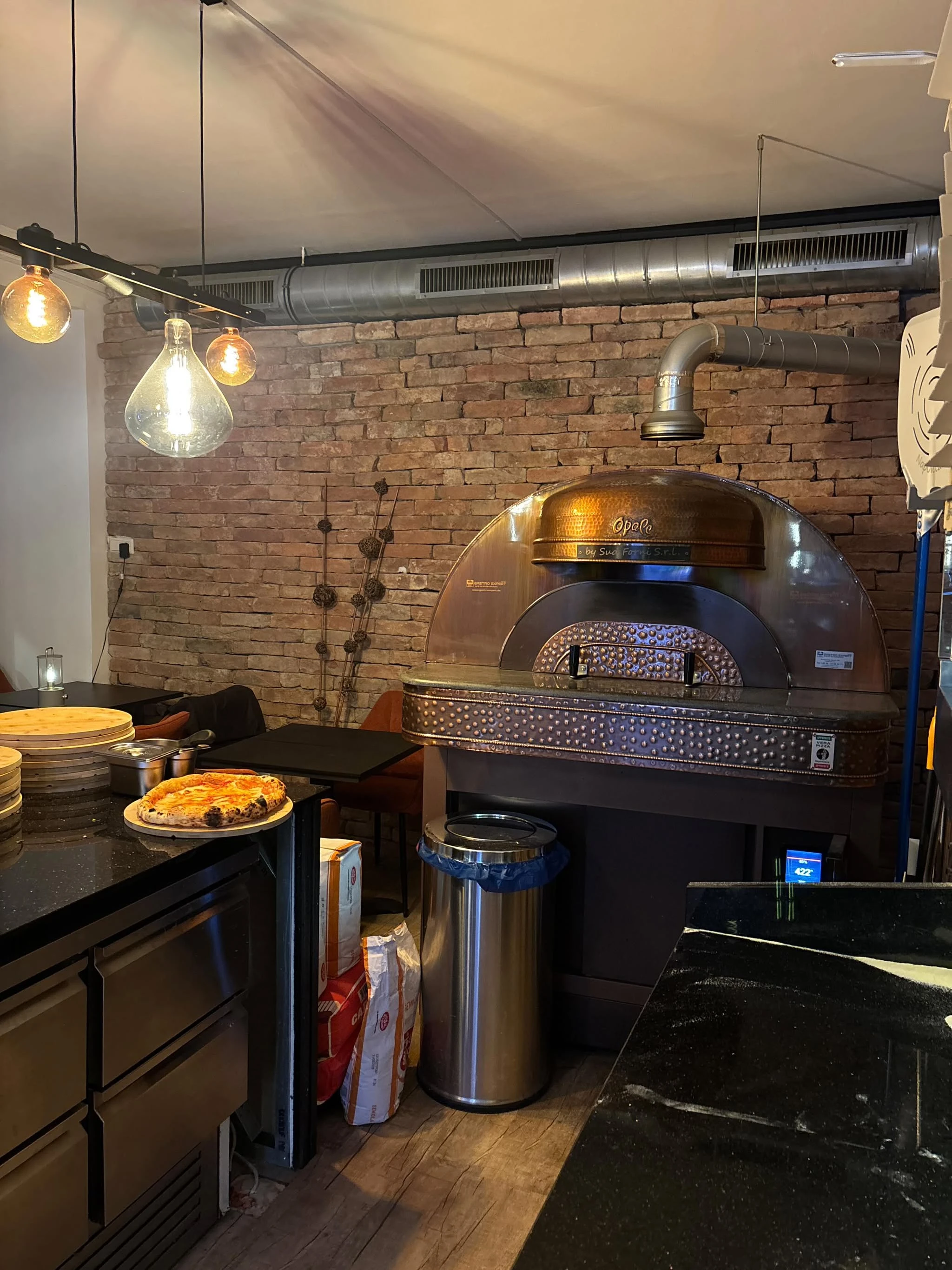 Professionelle Pizzeria mit Pizzaofen, frisch gebackener Pizza und Zutaten.